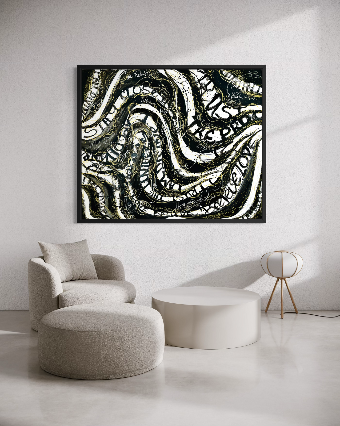 A framed abstract wall art print with black, white, and gray wavy patterns, displayed in a modern living room setting above a beige armchair and ottoman.