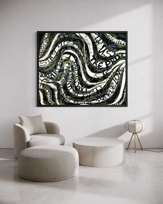 A framed abstract wall art print with black, white, and gray wavy patterns, displayed in a modern living room setting above a beige armchair and ottoman.