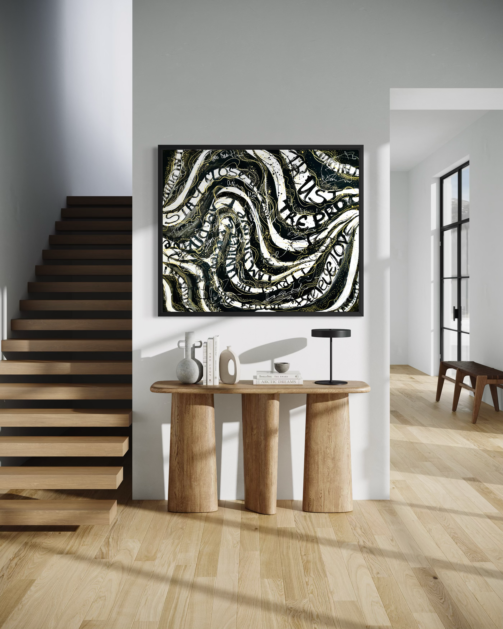 Abstract black and white canvas wall art with swirling organic patterns, displayed in a modern interior setting above a wooden console table next to a staircase.
