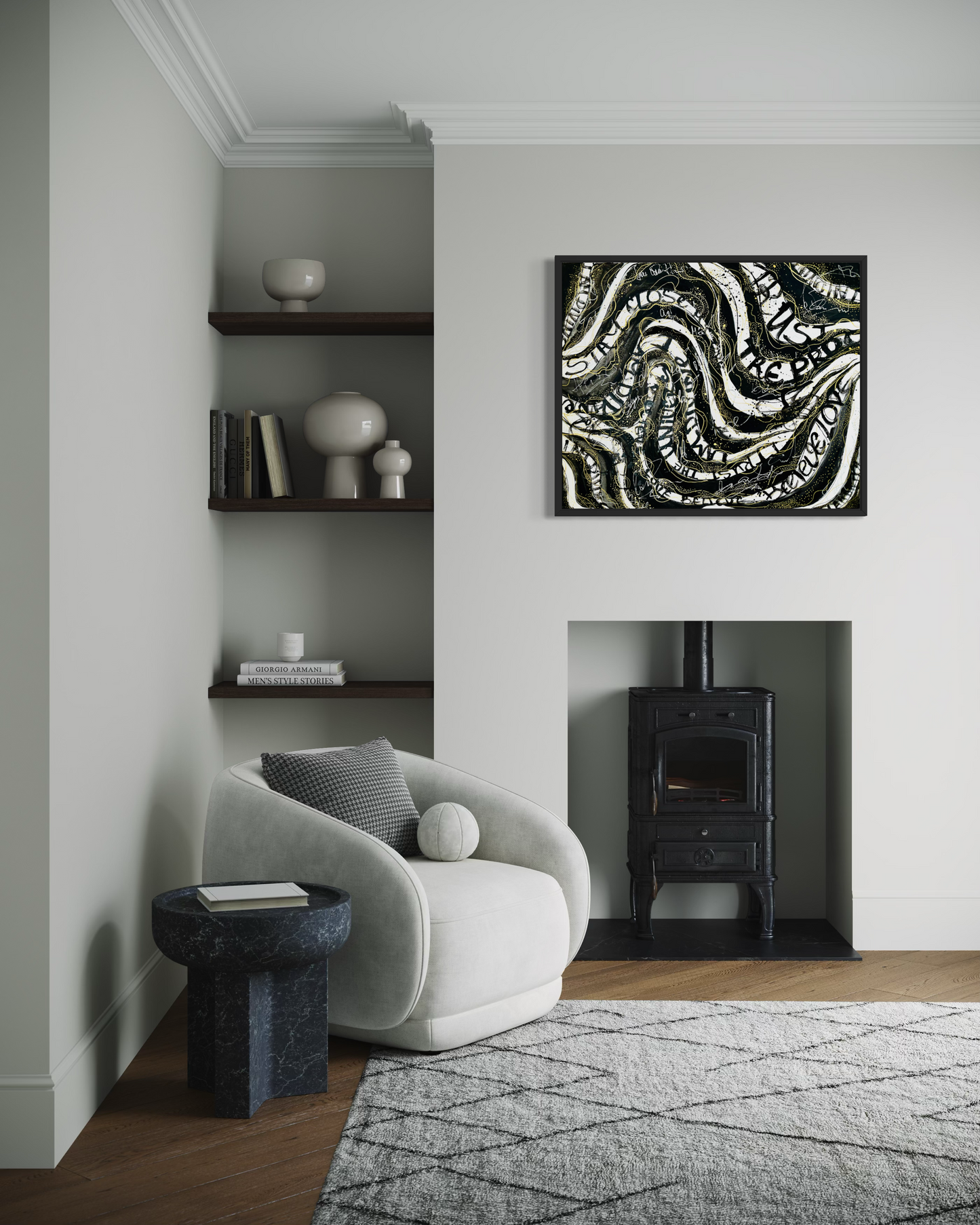 A styled interior room with a white curved armchair, dark wood shelves, a black wood-burning stove, a patterned rug, and a framed abstract black-and-white artwork on the wall above the stove.