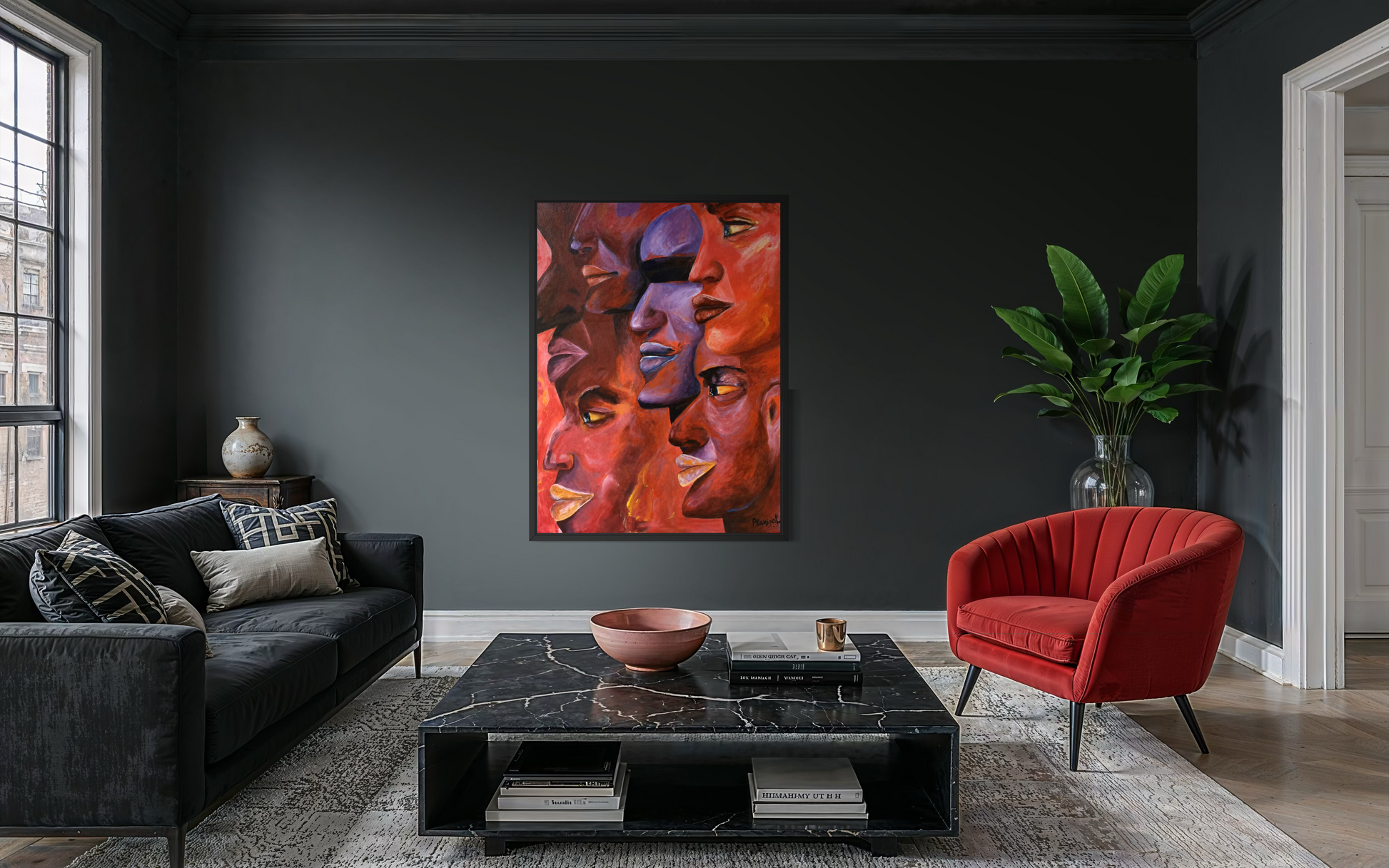 A framed abstract painting featuring stylized faces in warm red, orange, and purple tones, displayed on a dark charcoal wall in a modern living room setting with a black sofa, red armchair, and black coffee table.