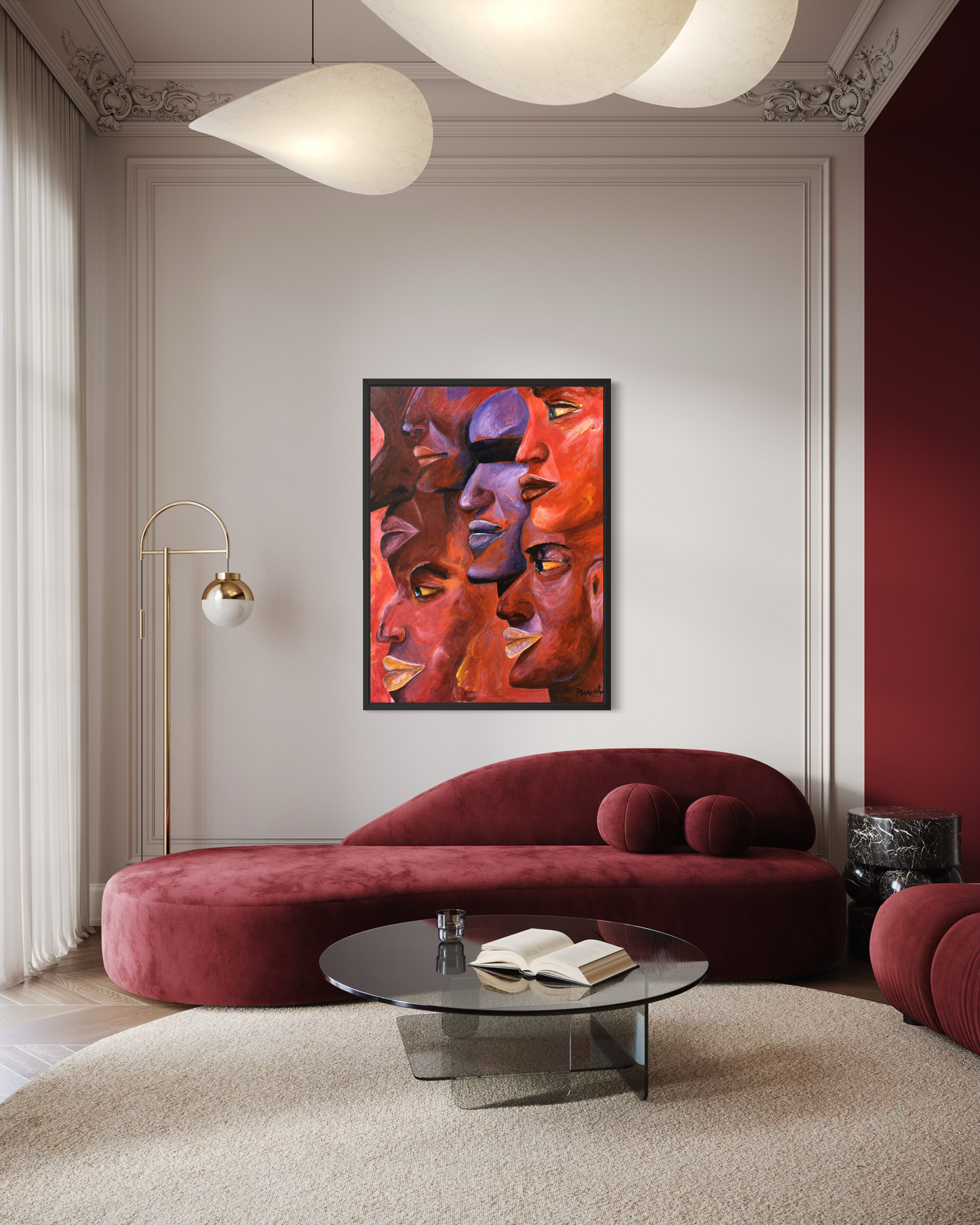 A framed abstract canvas print featuring a stylized face in warm red, orange, and purple tones, displayed on a light gray wall above a modern curved burgundy sofa in a styled living room.