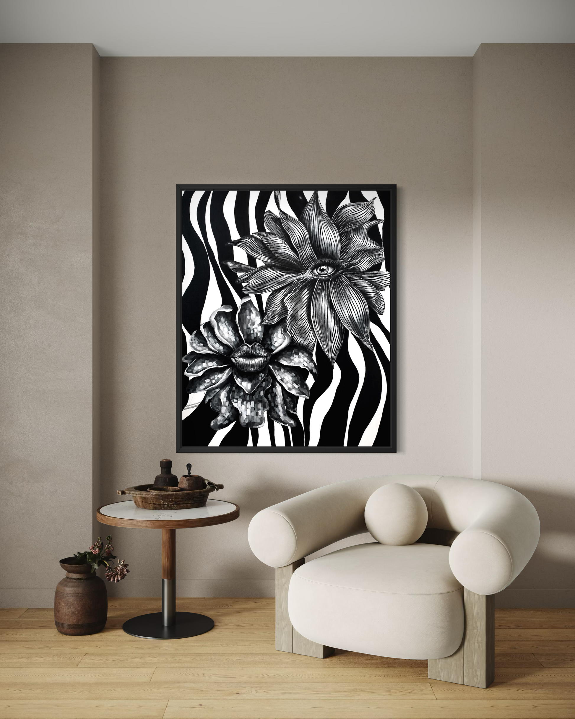 A framed black and white floral art print with zebra-like stripes hangs on a beige wall above a cream-colored modern armchair and a small round side table in a minimalist room setting.