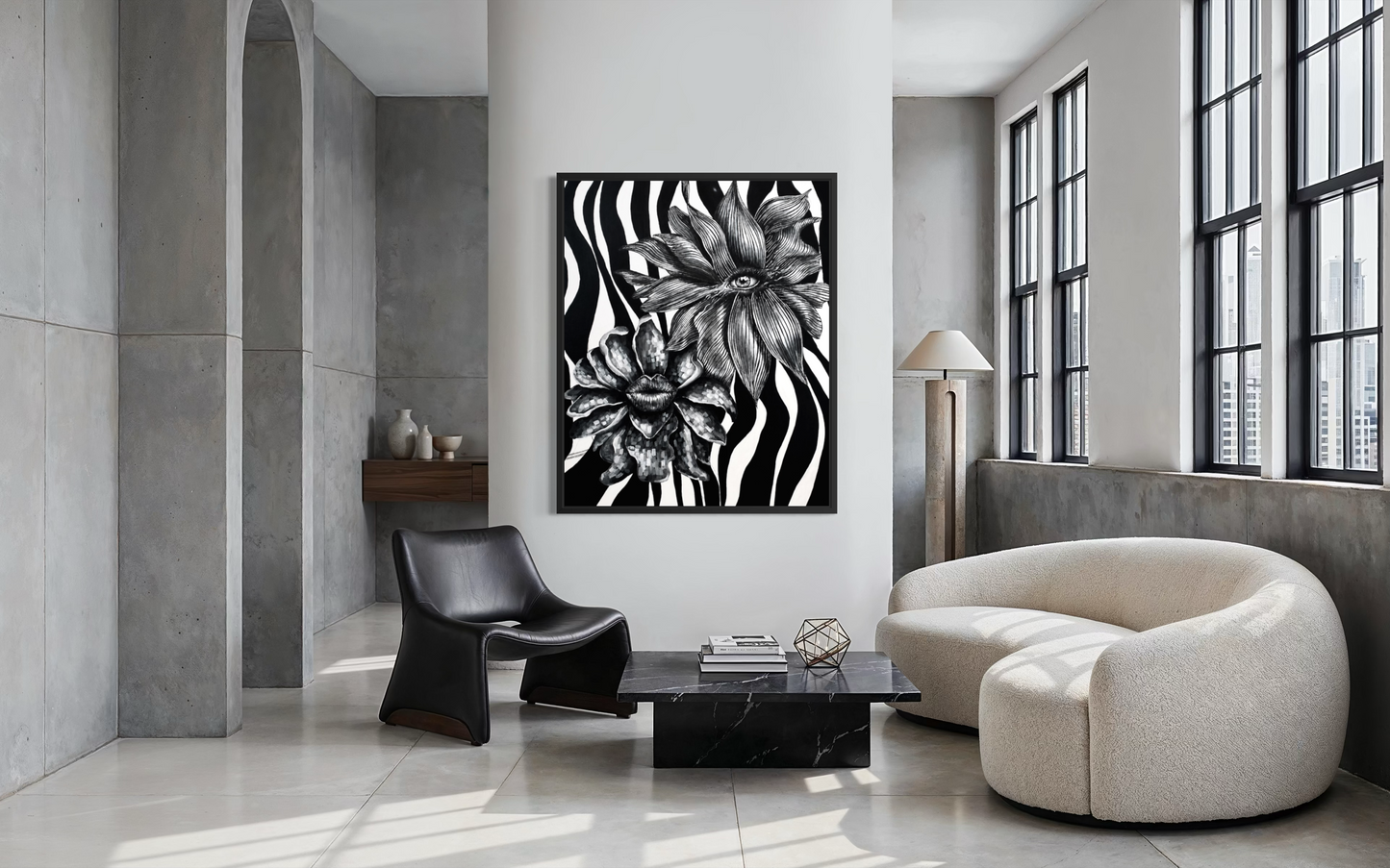 A framed black and white floral wall art print hangs on a white wall in a modern, minimalist living room with concrete walls, a cream-colored curved sofa, and a black accent chair.