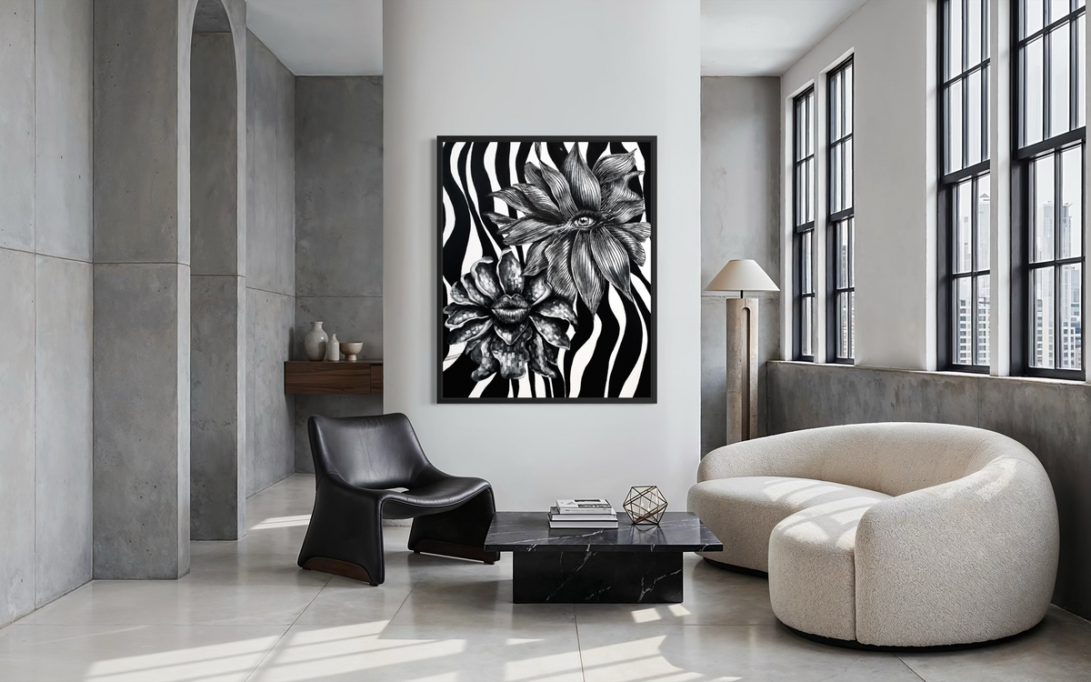 A framed black and white floral wall art print hangs on a white wall in a modern, minimalist living room with concrete walls, a cream-colored curved sofa, and a black accent chair.