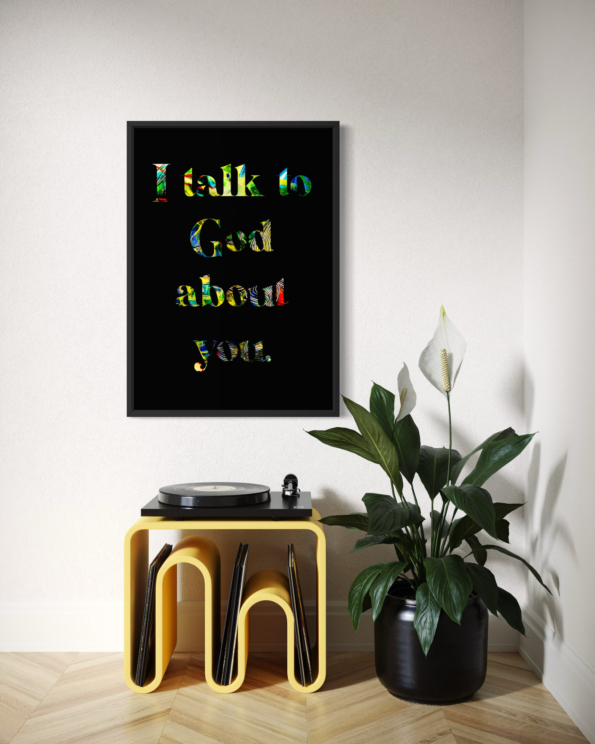 A framed wall art print with the text 'I talk to God about you.' in colorful lettering on a black background, displayed in a styled room above a yellow record stand and next to a potted plant.