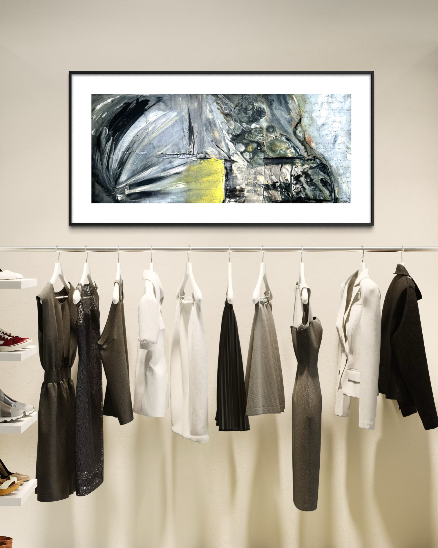 A framed abstract canvas print with black, white, gray, and yellow brushstrokes hangs on a beige wall above a clothing rack displaying various women's dresses and blouses in neutral tones.