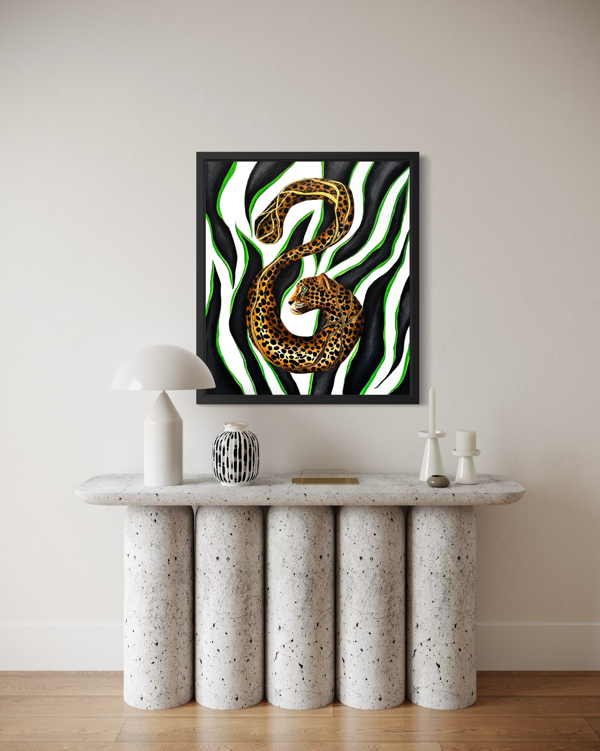 A framed wall art print featuring a leopard print snake coiled over a green and black zebra-stripe background, displayed above a modern speckled stone console table in a minimalist room.